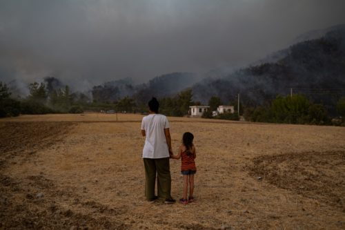 A woman and child stand in a field as they watch wildfires as they burn in Koycegiz district of Mugla on August 3, 2021.